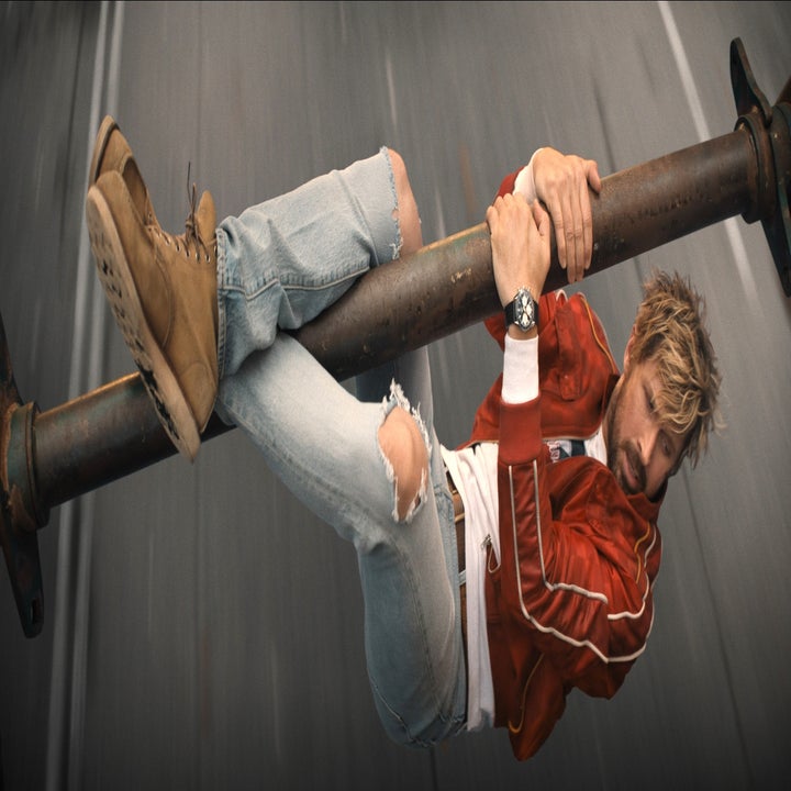 Person in a red jacket and ripped jeans hangs onto a large pole, appearing in a dynamic action scene