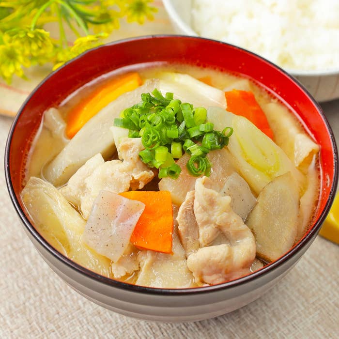 豚汁のボウルに、具材として豚肉、ニンジン、ネギ、こんにゃくが入っている。上にネギがトッピングされている。