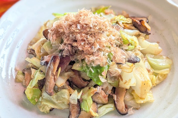 キャベツとシイタケの炒め物。上に鰹節がのせられています。シンプルな白い皿に盛り付けられ、おいしそうに見えます。