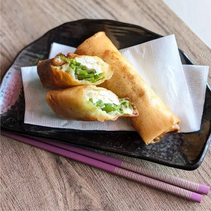 黒い皿に盛られた春巻き2本。1本は半分にカットされ、具材が見える。隣にピンクの箸が置かれている。