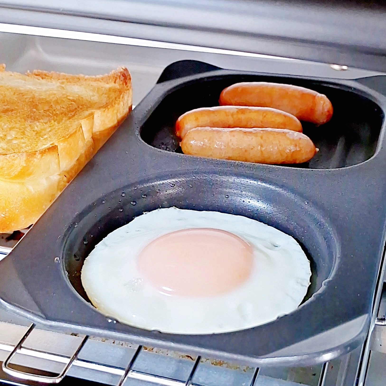 電気オーブンでトースト、目玉焼き、ソーセージを同時に調理している様子。