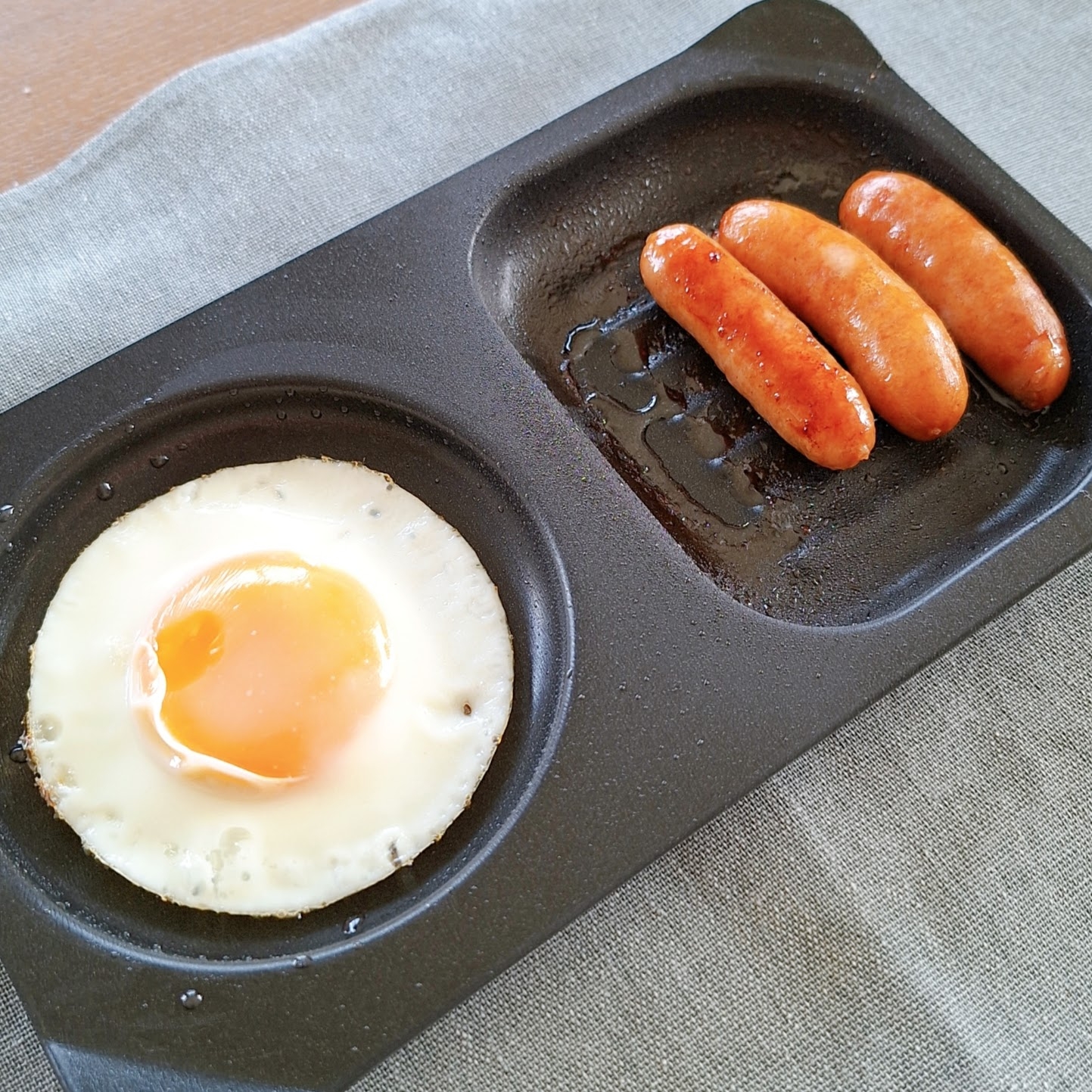 目玉焼きとソーセージ3本がトレイに載っている朝食シーン。