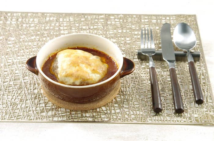 グラタン皿に入った焼きカレーがテーブルマット上に置かれ、横にカトラリーセットが配置されています。