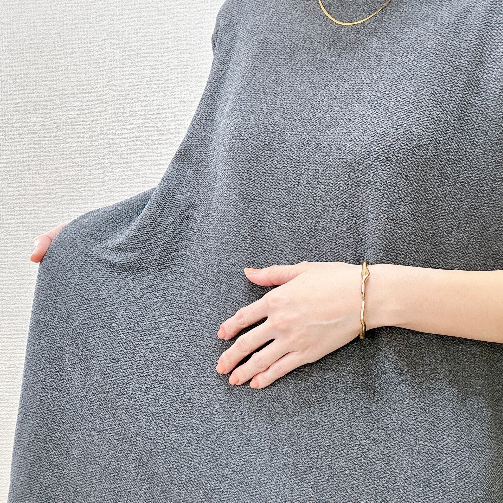 女性がシンプルなドレスを着て、片手でお腹を優しく抑えている。シンプルなアクセサリーを身につけている。