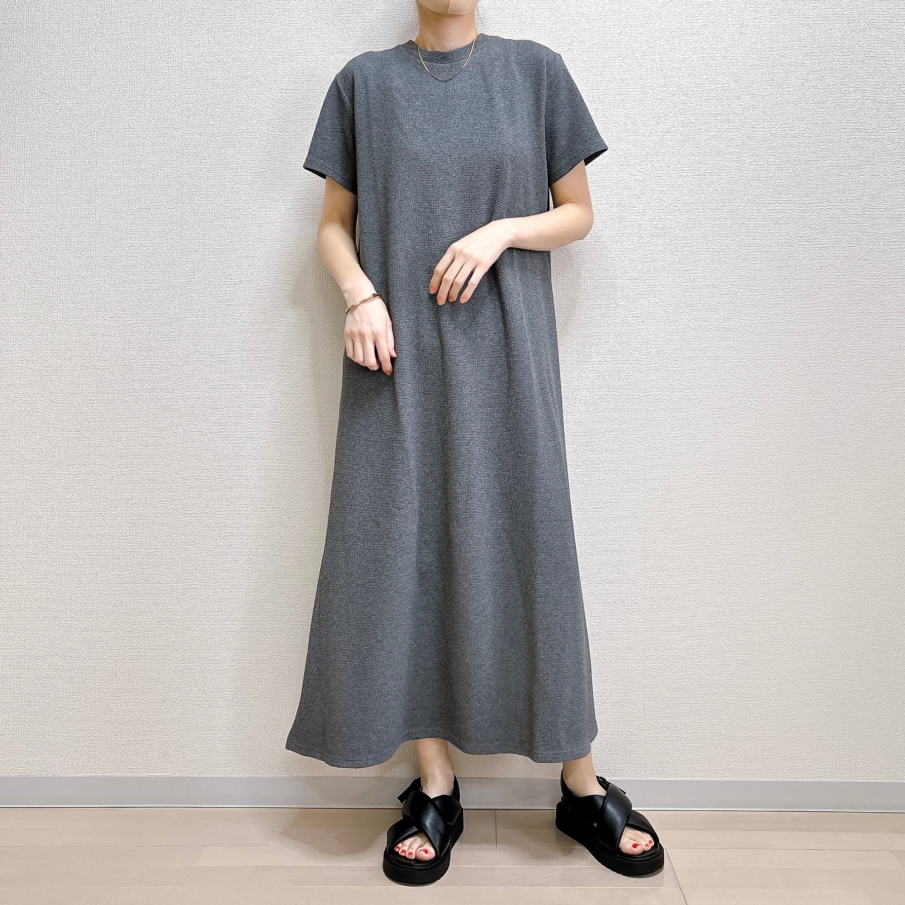 女性が着る、ゆったりとしたシンプルなロングTシャツドレスにサンダルを合わせたカジュアルなスタイル。