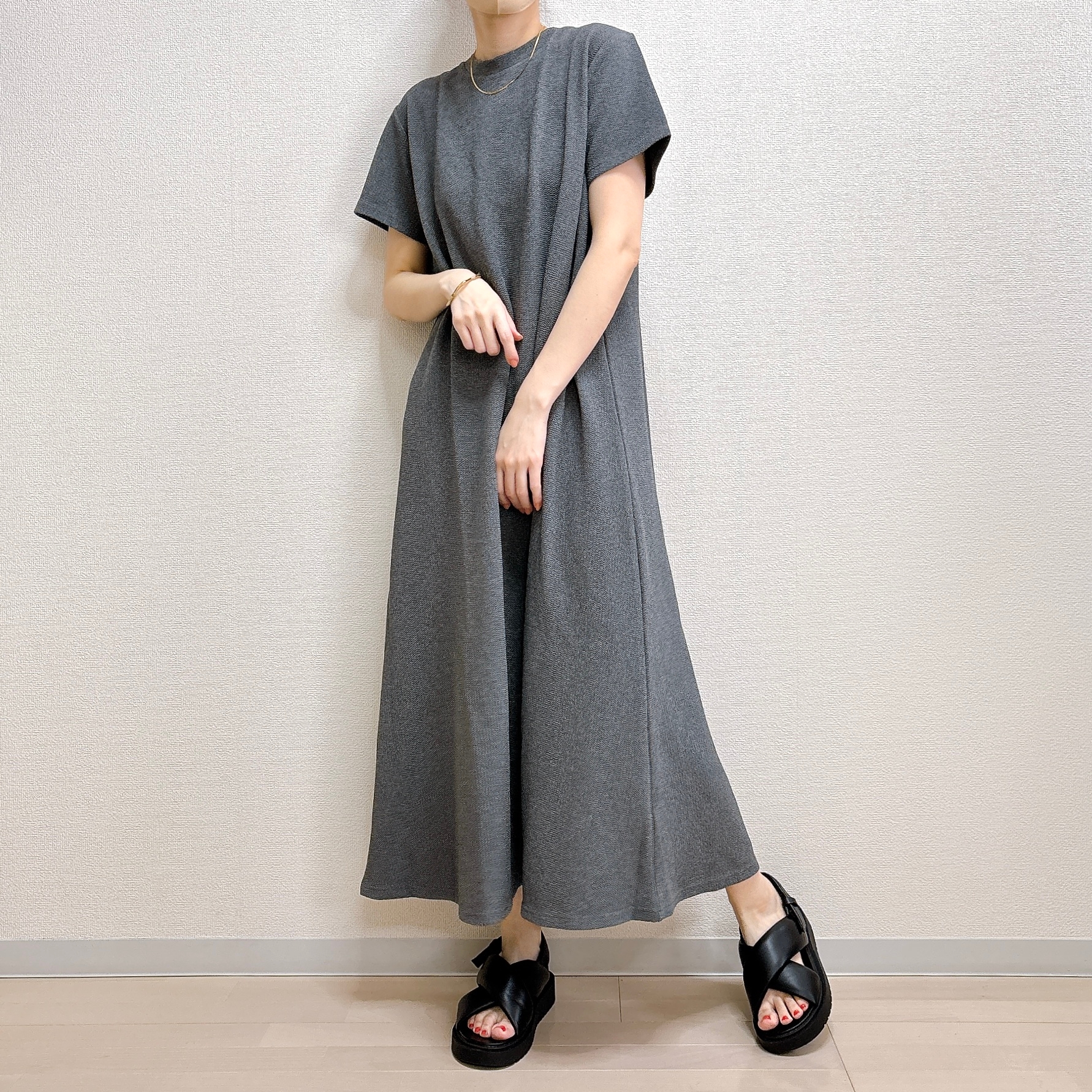 女性がシンプルなロングワンピースとサンダルを着用してポーズをとっている。