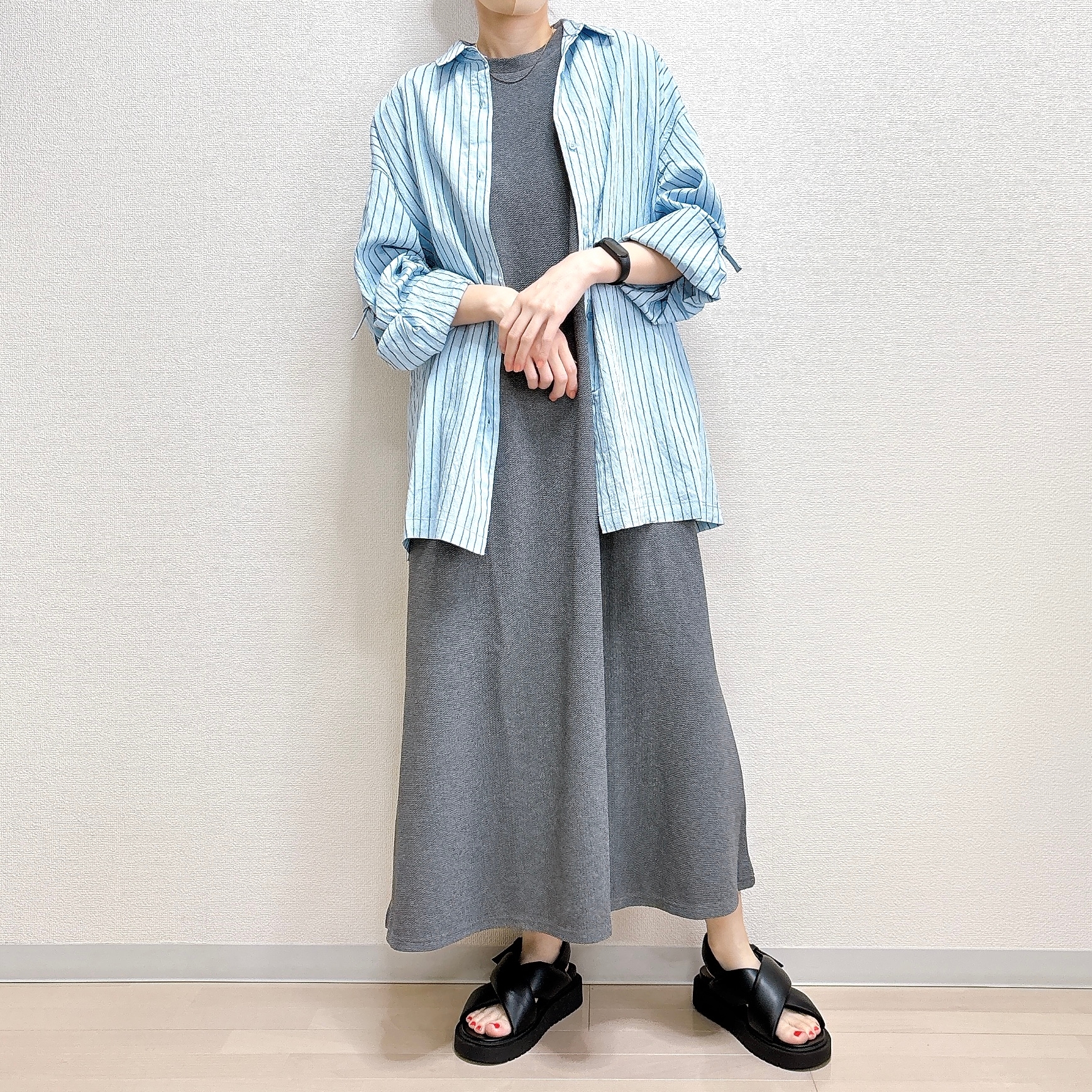 人物がカジュアルな長いスカートとストライプシャツを着用しポーズをとっている。