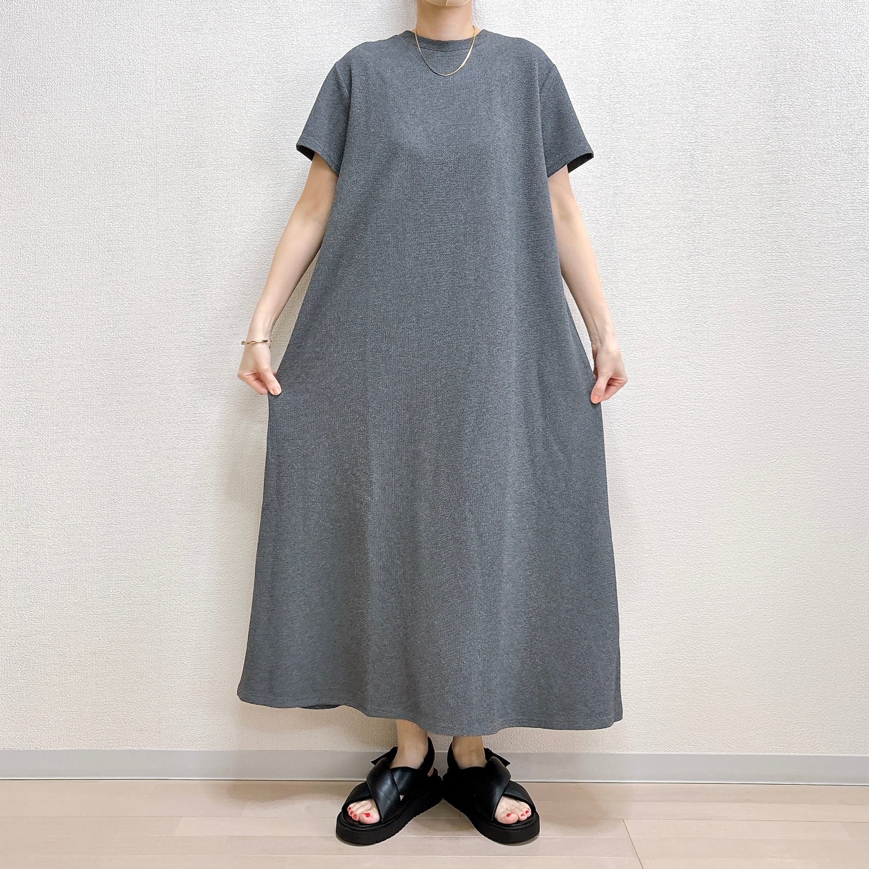 ゆったりしたシンプルなワンピースを着た人物が、サンダルを履いて立っています。