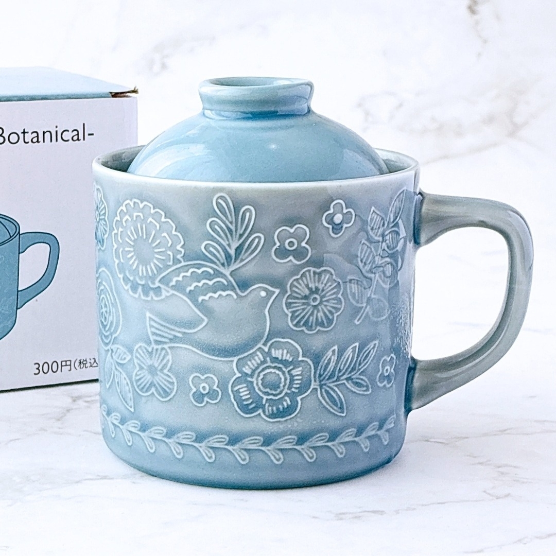 鳥と植物のデザインが施された陶器のカップと蓋。背景には同じデザインのパッケージが見える。