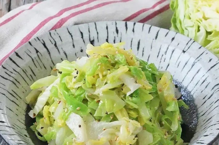 キャベツのサラダが木製のテーブルに置かれたお皿に盛り付けられている。背景に布巾が見える。