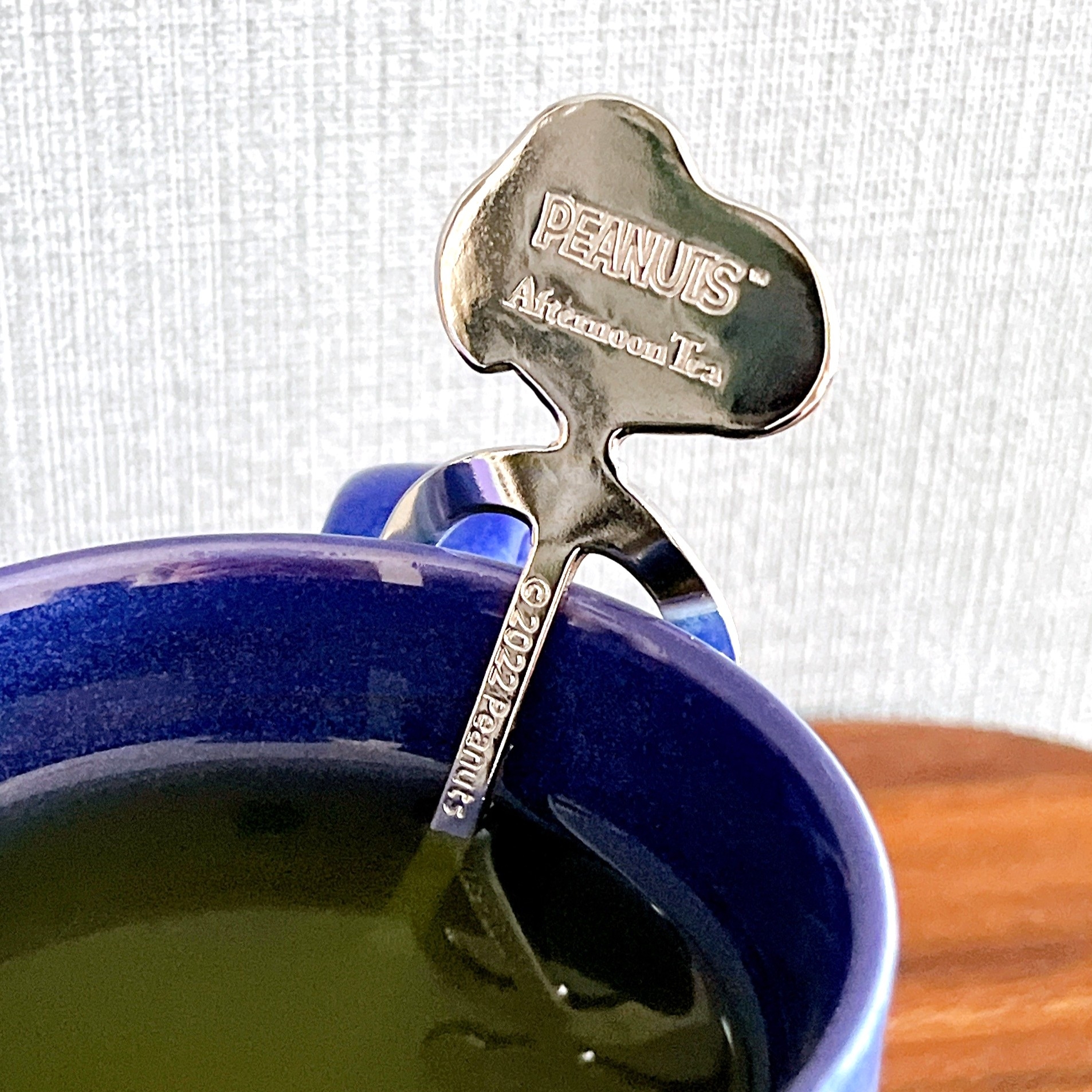 カップにティースプーンがかかっており、スプーンに「PEANUTS Afternoon Tea」と刻まれている。