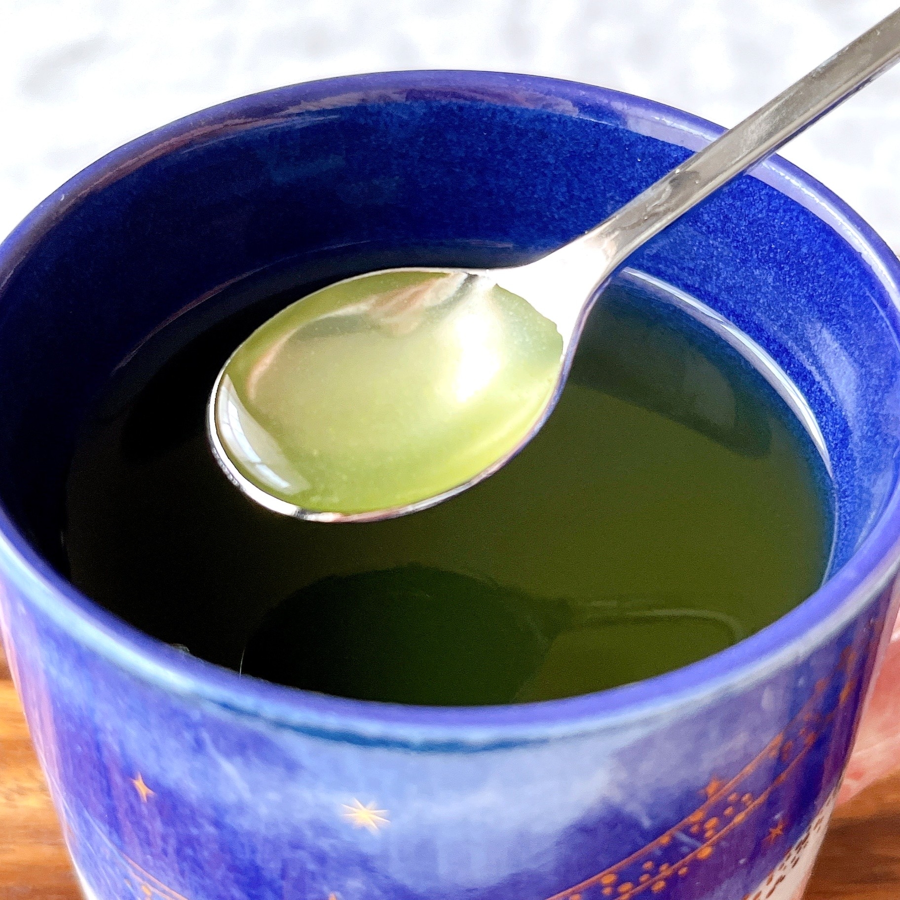 青いカップに濃い緑色の飲み物が入っており、スプーンですくわれています。
