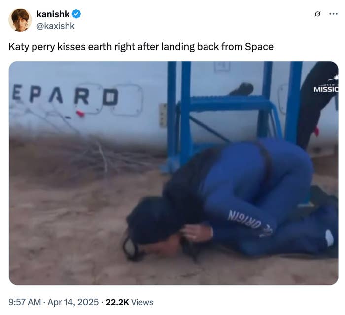 Person in a space suit kneels and kisses the ground after landing, with space equipment visible in the background