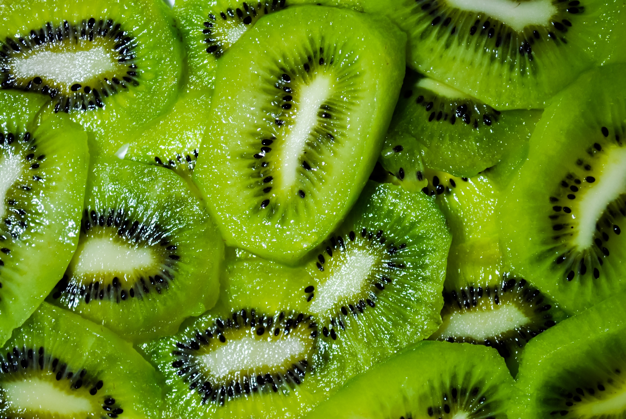 Slices of kiwi fruit piled closely together, highlighting their distinctive seedy patterns
