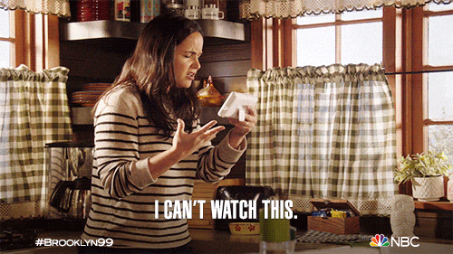 Woman in a kitchen intensely watching a phone, wearing a striped sweater; text says "I CAN'T WATCH THIS."