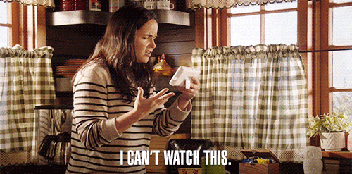 Woman in a kitchen intensely watching a phone, wearing a striped sweater; text says "I CAN'T WATCH THIS."
