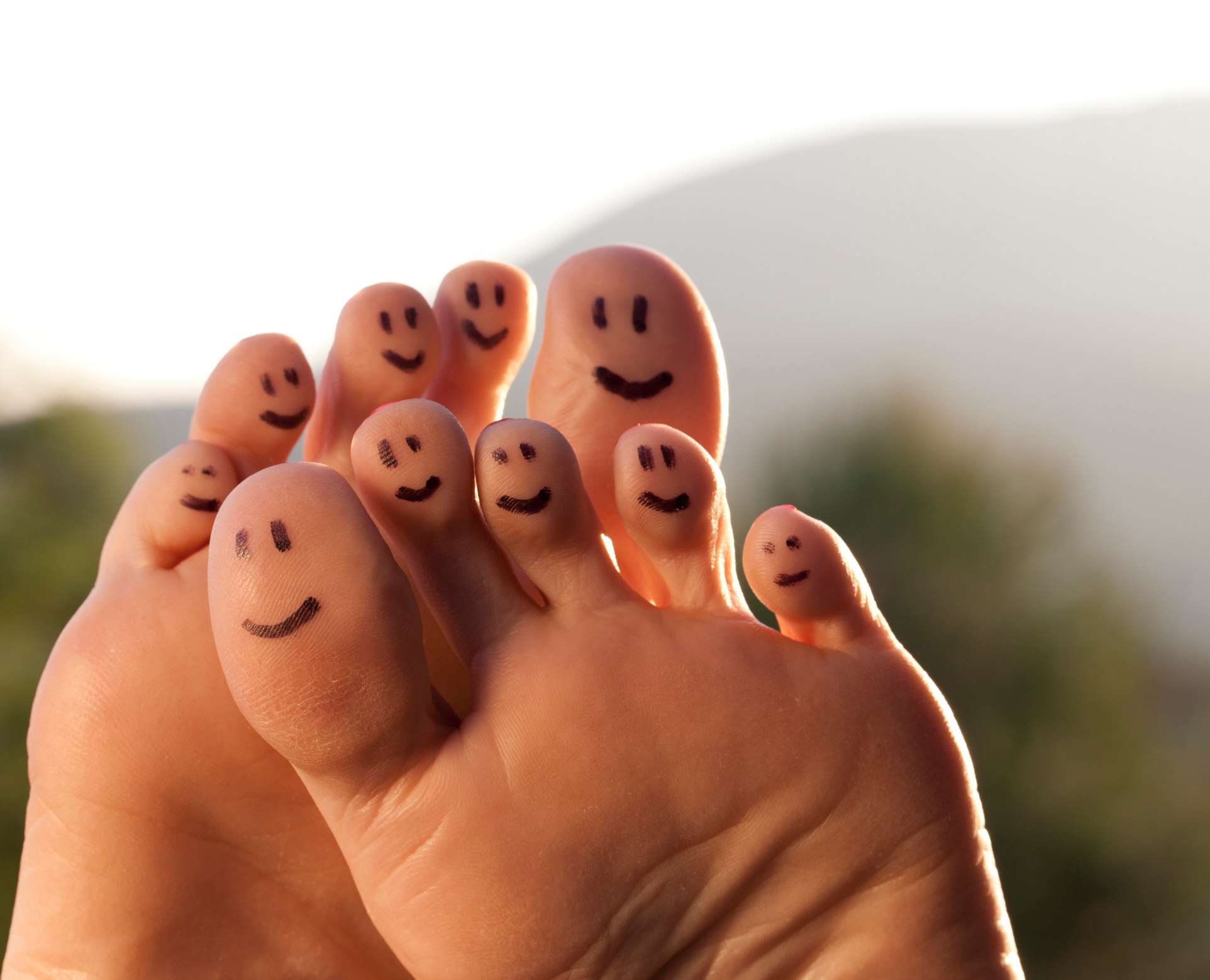 Smiling faces drawn on toes with a scenic outdoor background