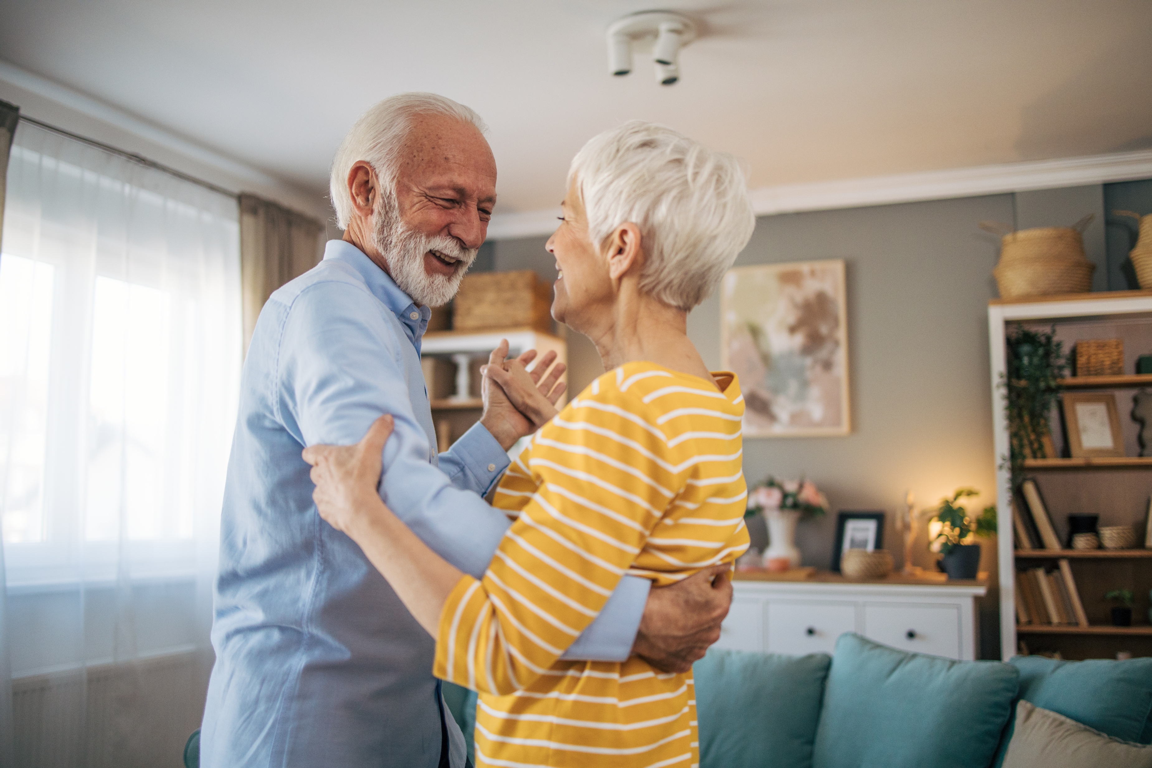 Elderly couple dancing joyfully in a cozy living room, sharing a loving moment together