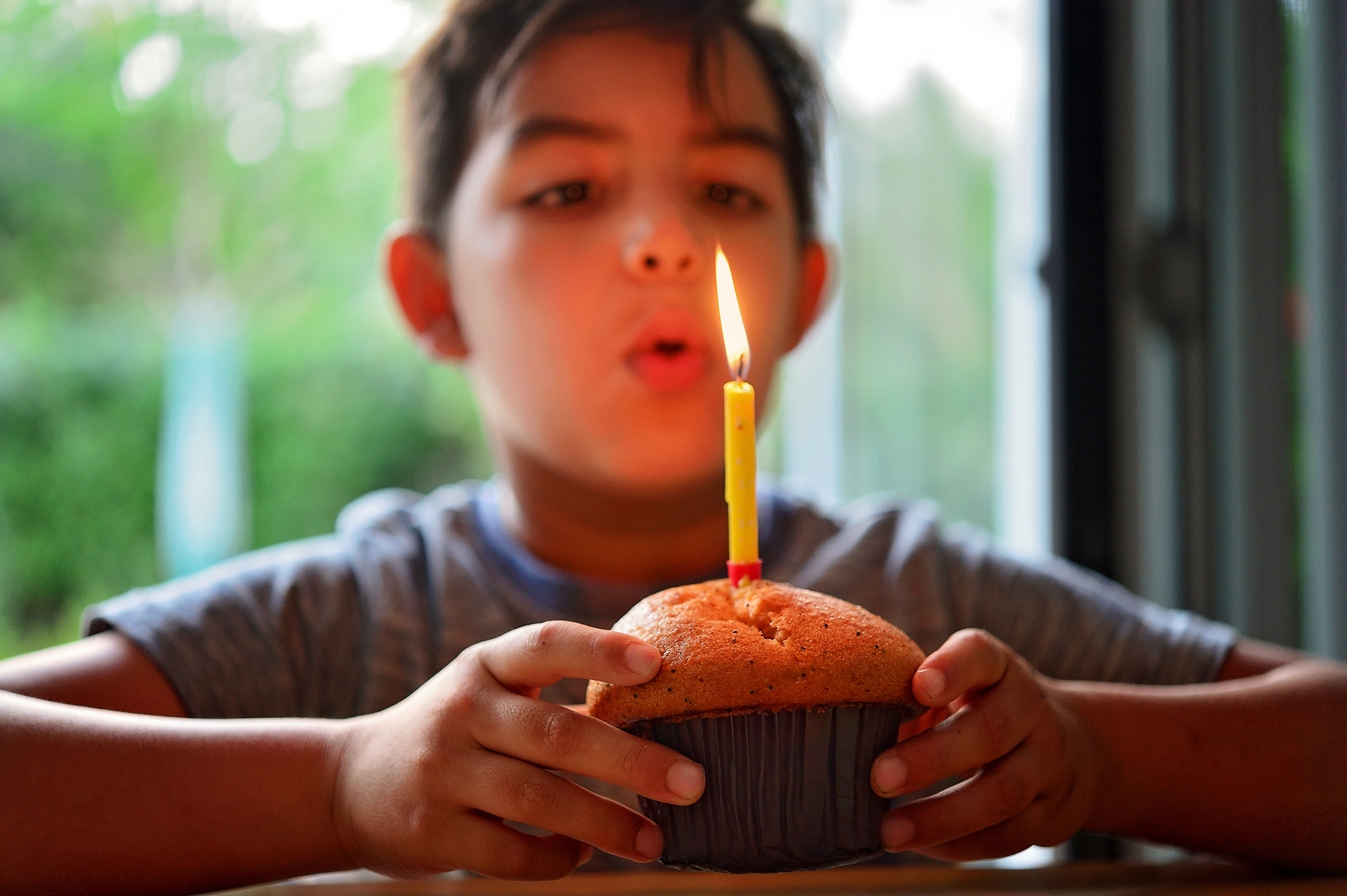 Child blowing out a lit candle on a cupcake, making a wish