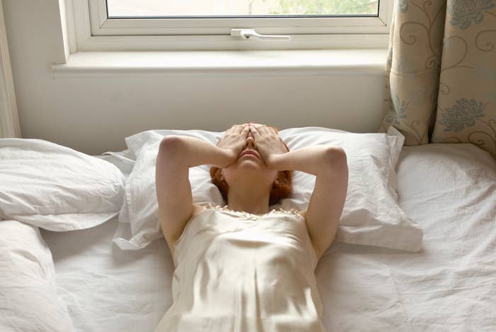 Person lying in bed in a relaxed position with hands over eyes, appearing to wake up or rest