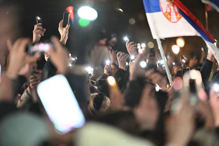 Crowd holding smartphones with flashlights on at night, waving a flag