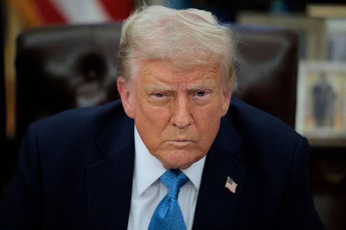 I don't know who this is. A person is wearing a suit with a U.S. flag pin, seated, looking directly at the camera with a serious expression