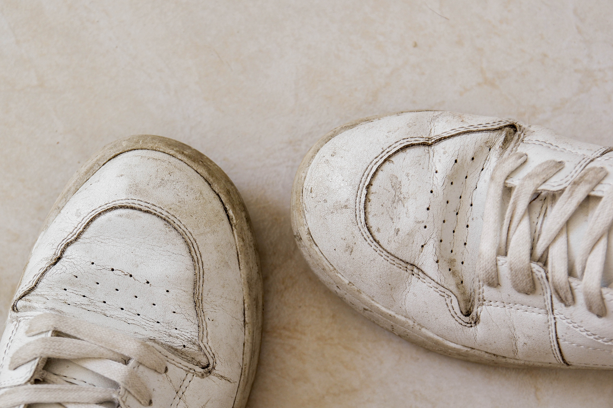 Worn white sneakers on a light floor, showing scuffs and signs of wear
