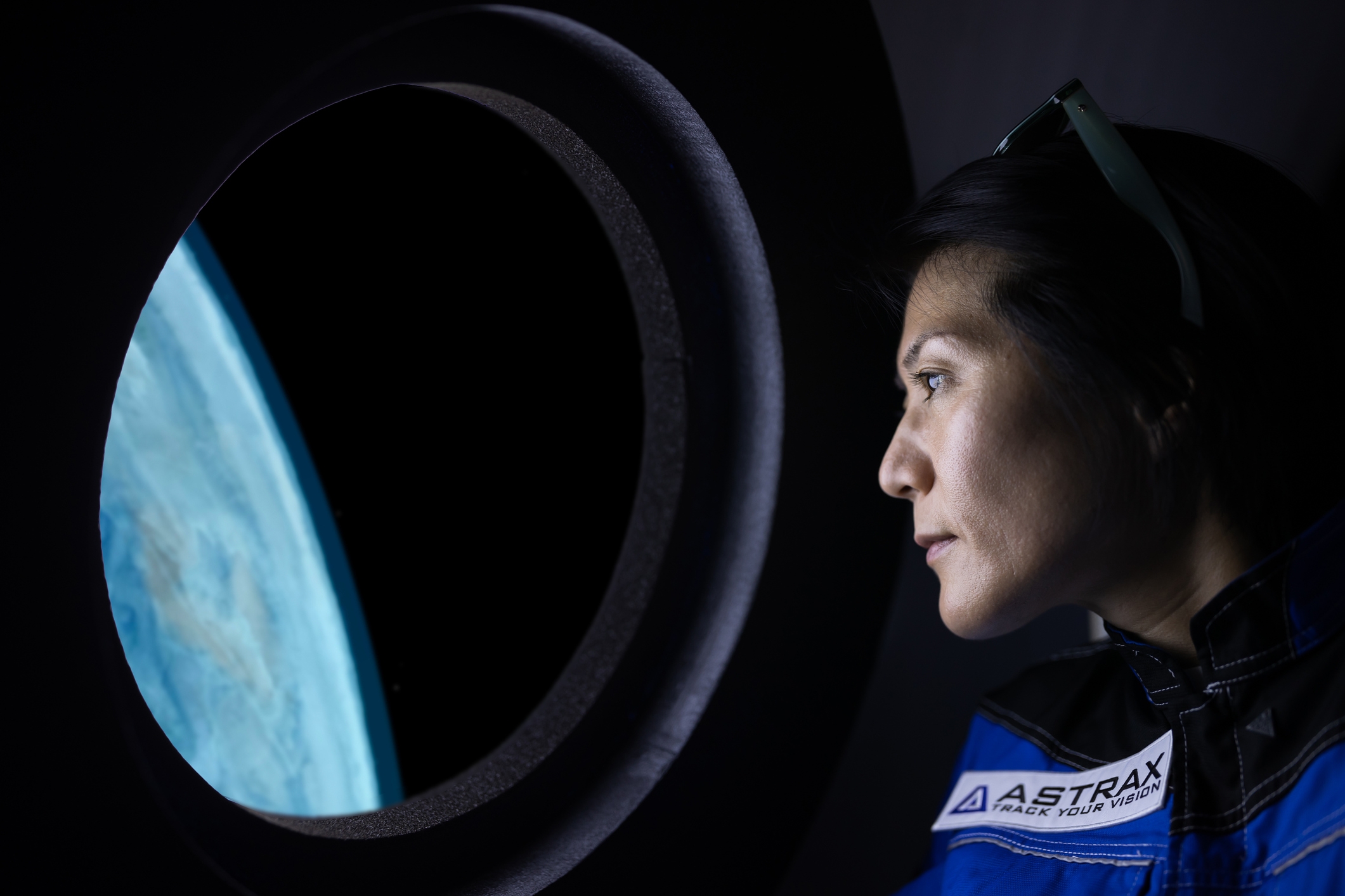 Person in a spacesuit gazes thoughtfully out spaceship window at Earth