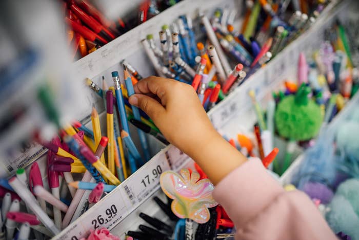 Hand selecting pens from a store display filled with various writing tools and prices