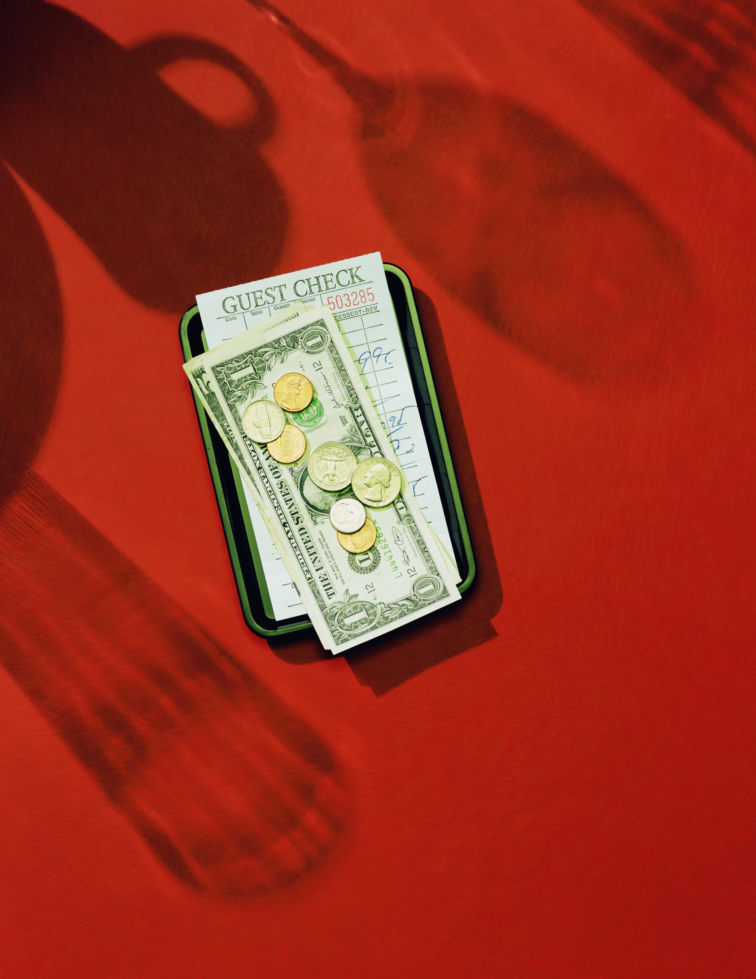 Guest check with money and coins on a tray, implying a restaurant tip, set against a plain table, highlighting financial transactions in service industry