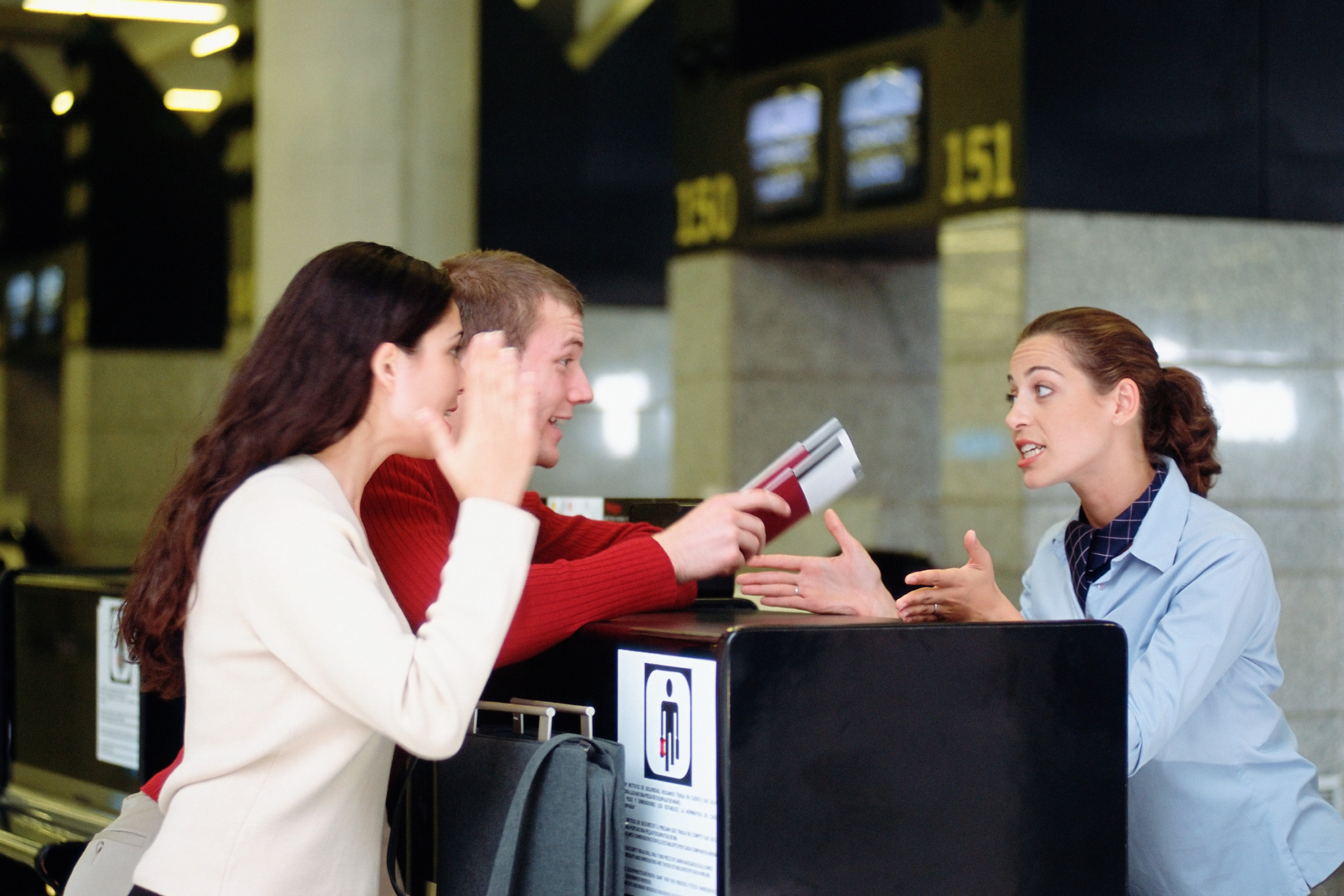 People discussing with an airline employee at a ticket counter, holding boarding passes. The scene suggests a travel-related issue or inquiry