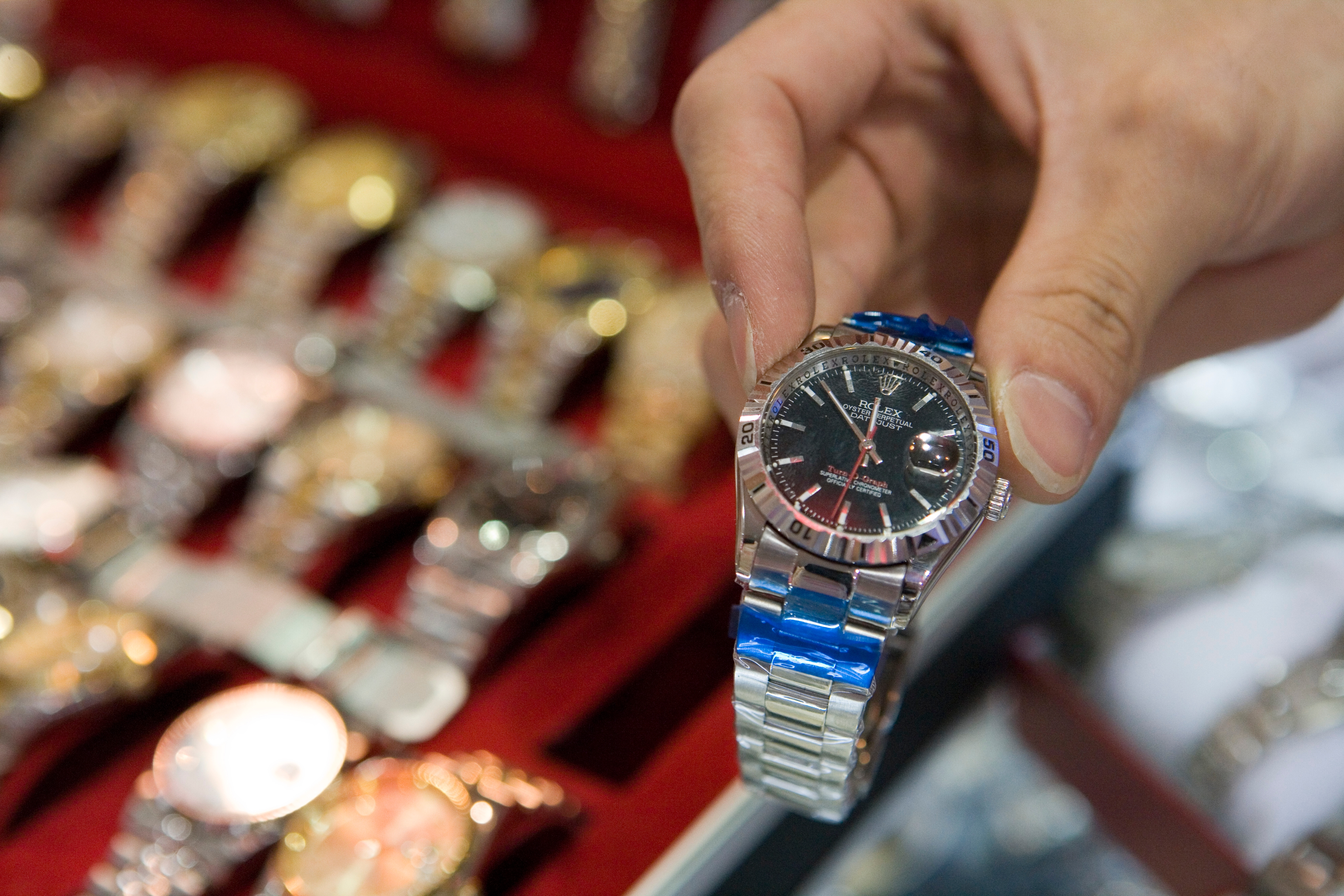 Person holding a luxury watch in a display case filled with various watches, highlighting choices in fine timepieces