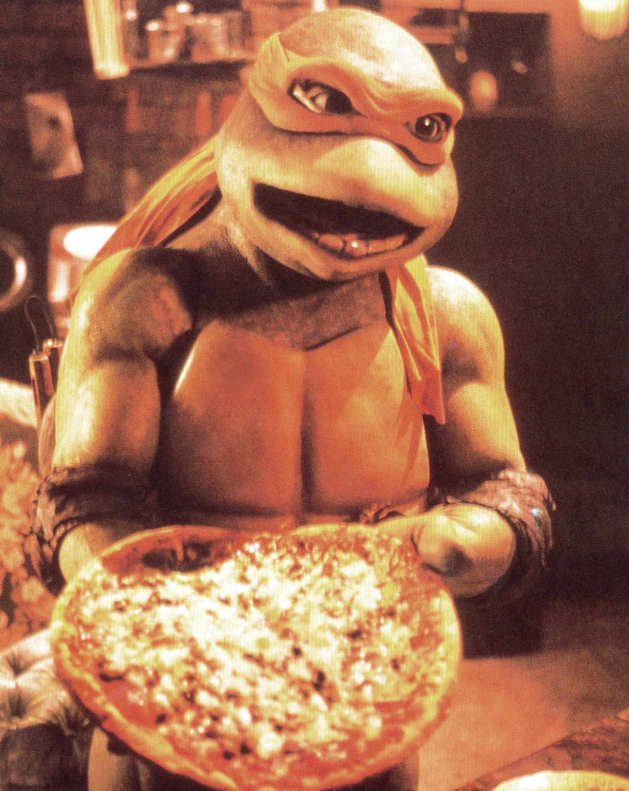 A Ninja Turtle character holds out a pizza with a smile, in a dimly lit setting