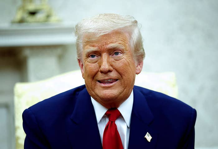 A person in a suit and red tie is sitting, looking slightly upwards