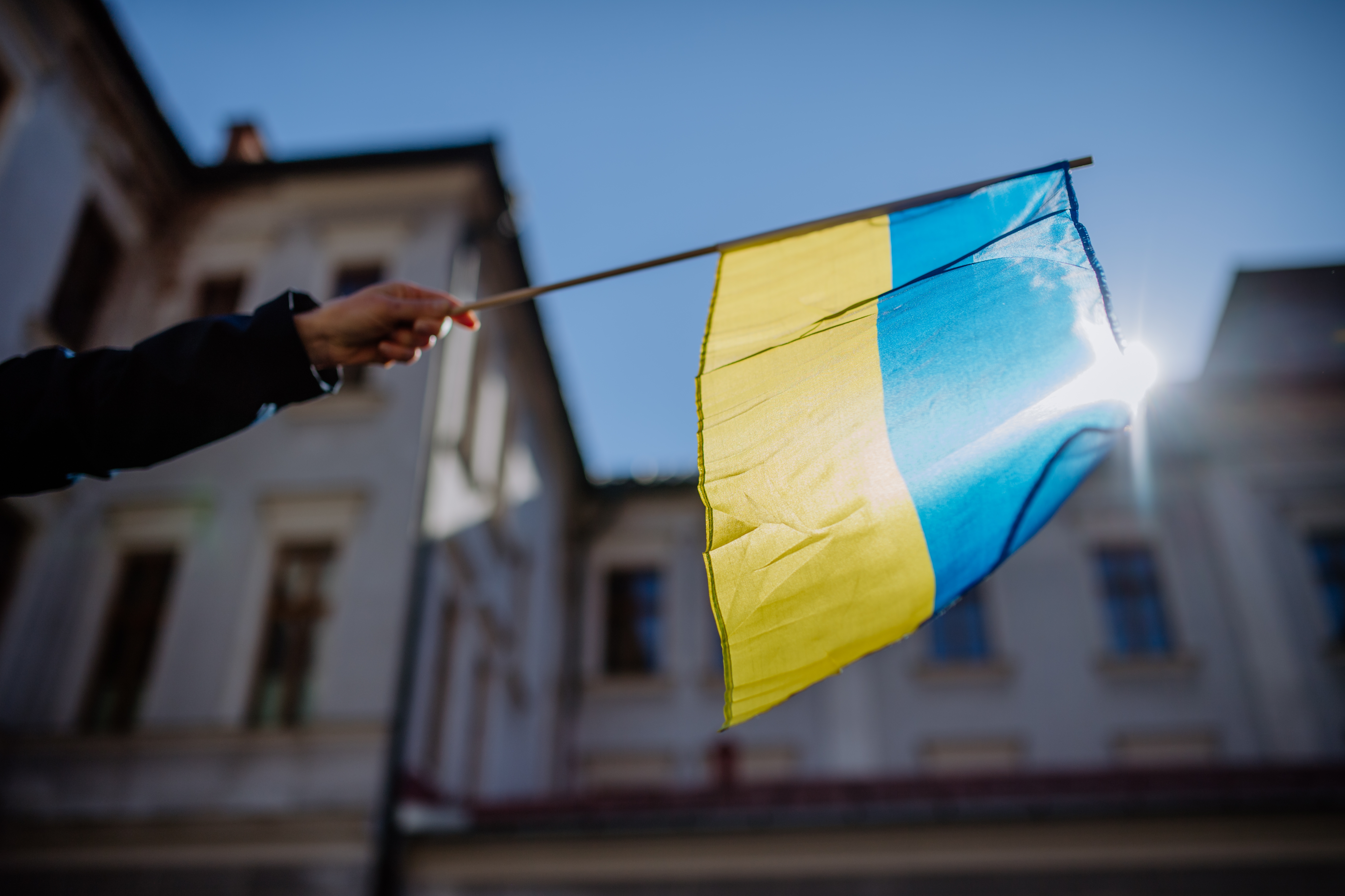 Hand holding a small Ukrainian flag against a building background
