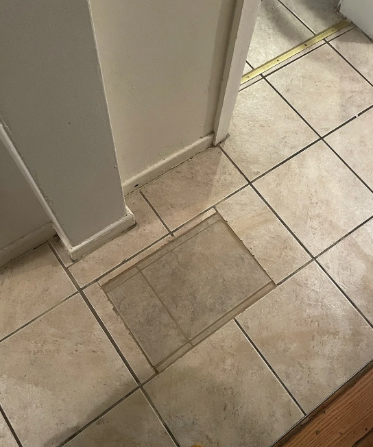 Tiled floor with a square pattern. Broken tiles are replaced with different rectangular tiles that don't line up