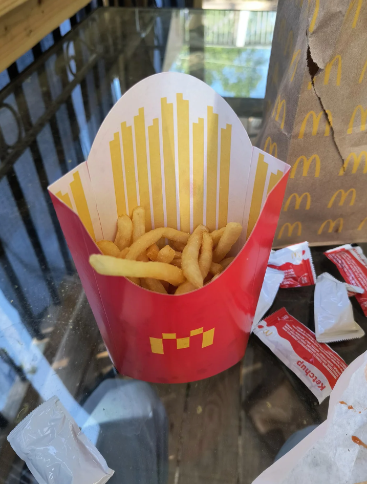 McDonald's fries are shown in a container placed on an outdoor table with additional packaging nearby