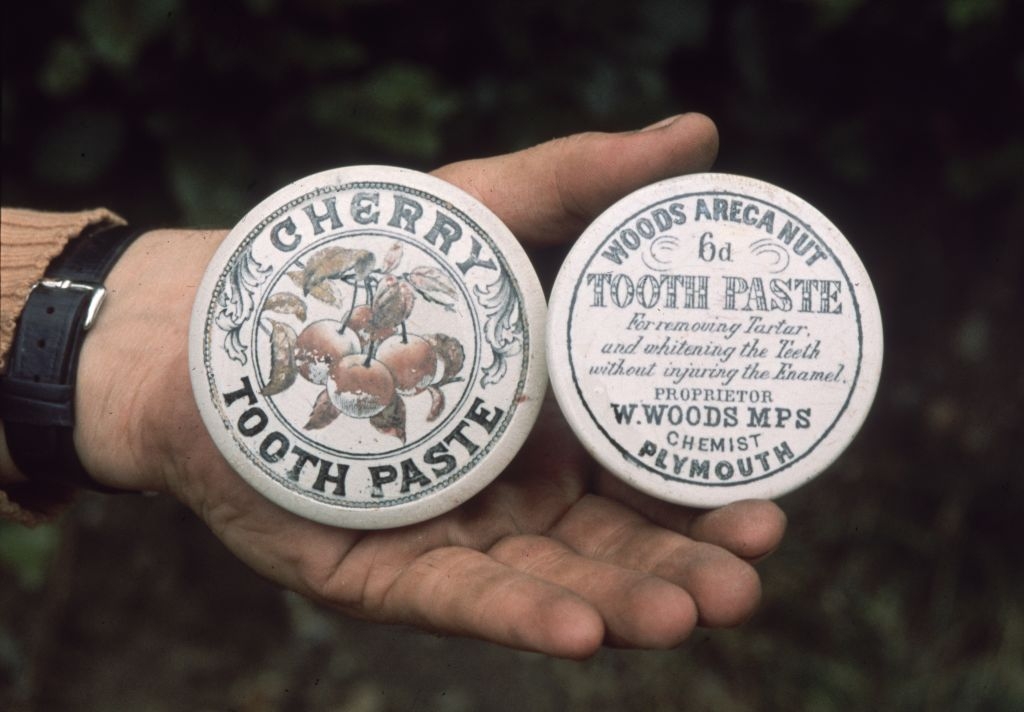 Vintage cherry toothpaste container held in a hand, featuring decorative fruit graphic and product details from W. Woods, chemist in Plymouth