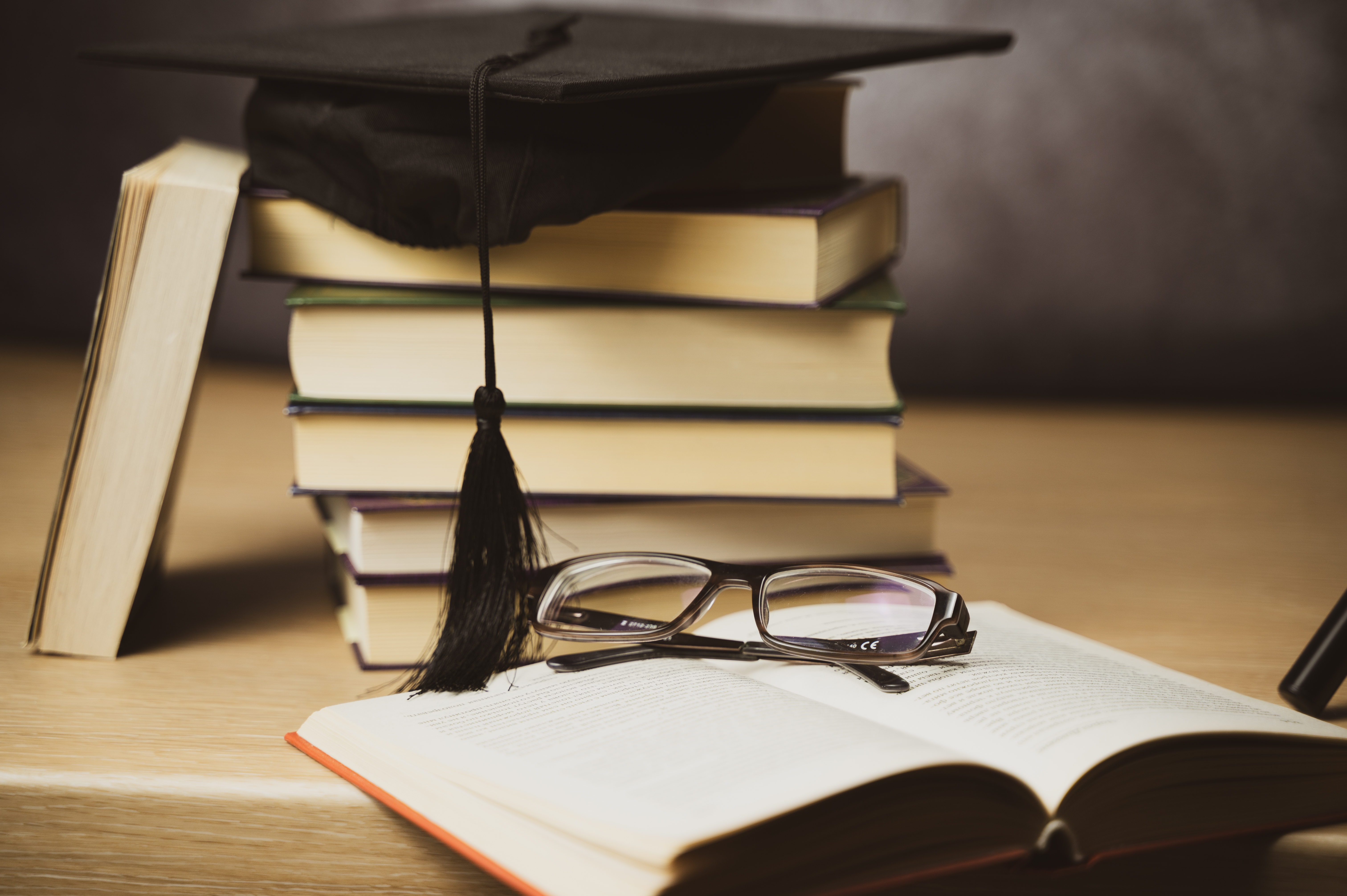 Graduation cap on stacked books with reading glasses on an open book, symbolizing education and learning