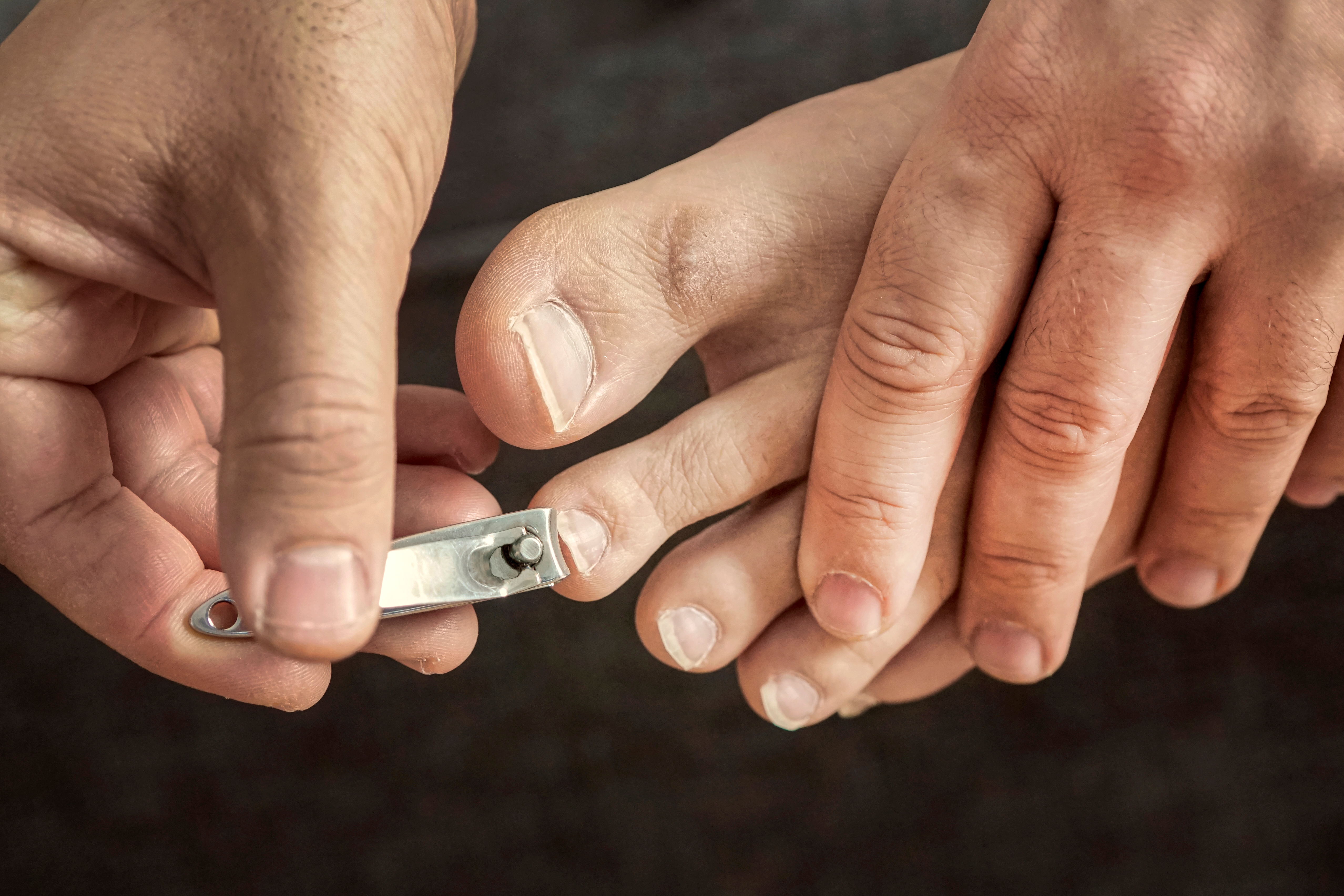 Person clipping toenails with a metal nail clipper, showing a close-up view of fingers and toes during the grooming process