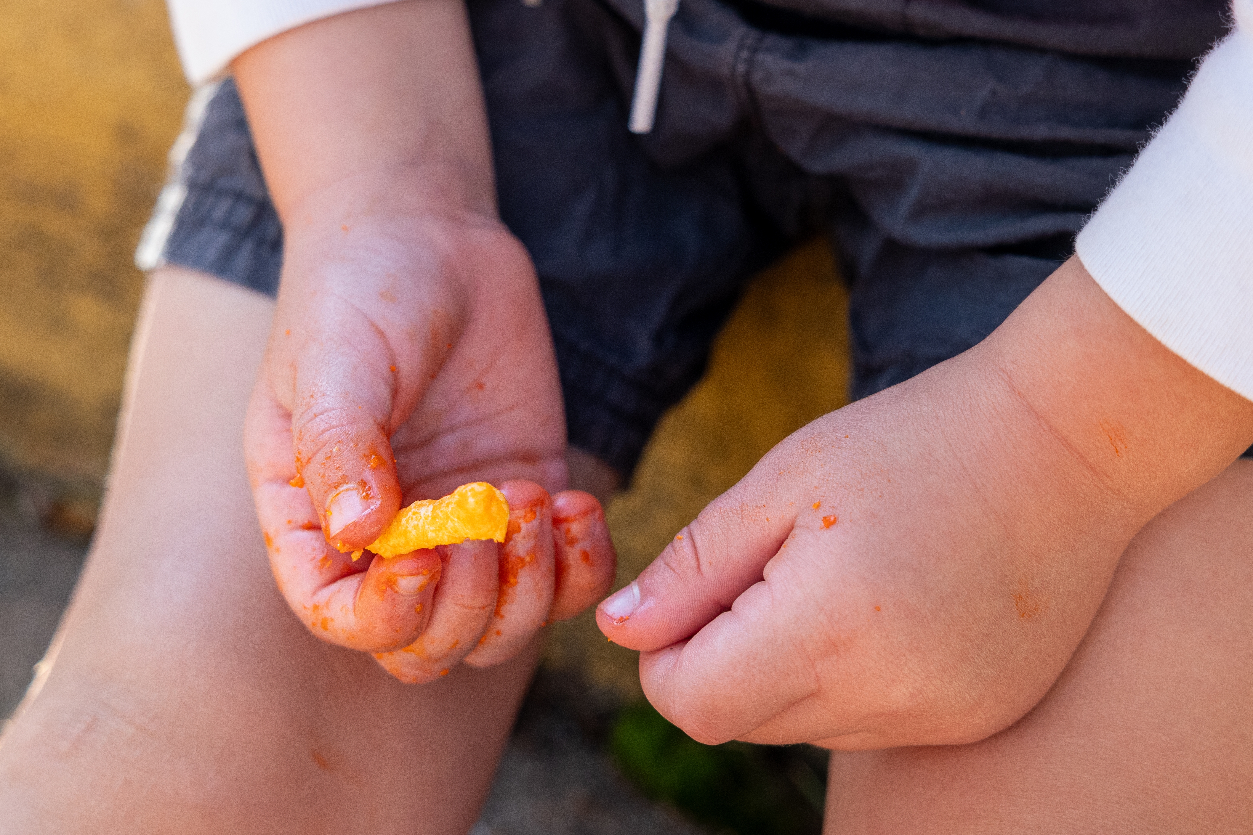 Child's hands holding a cheese-flavored snack, fingers covered in cheesy residue, suggesting a playful or casual snacking moment