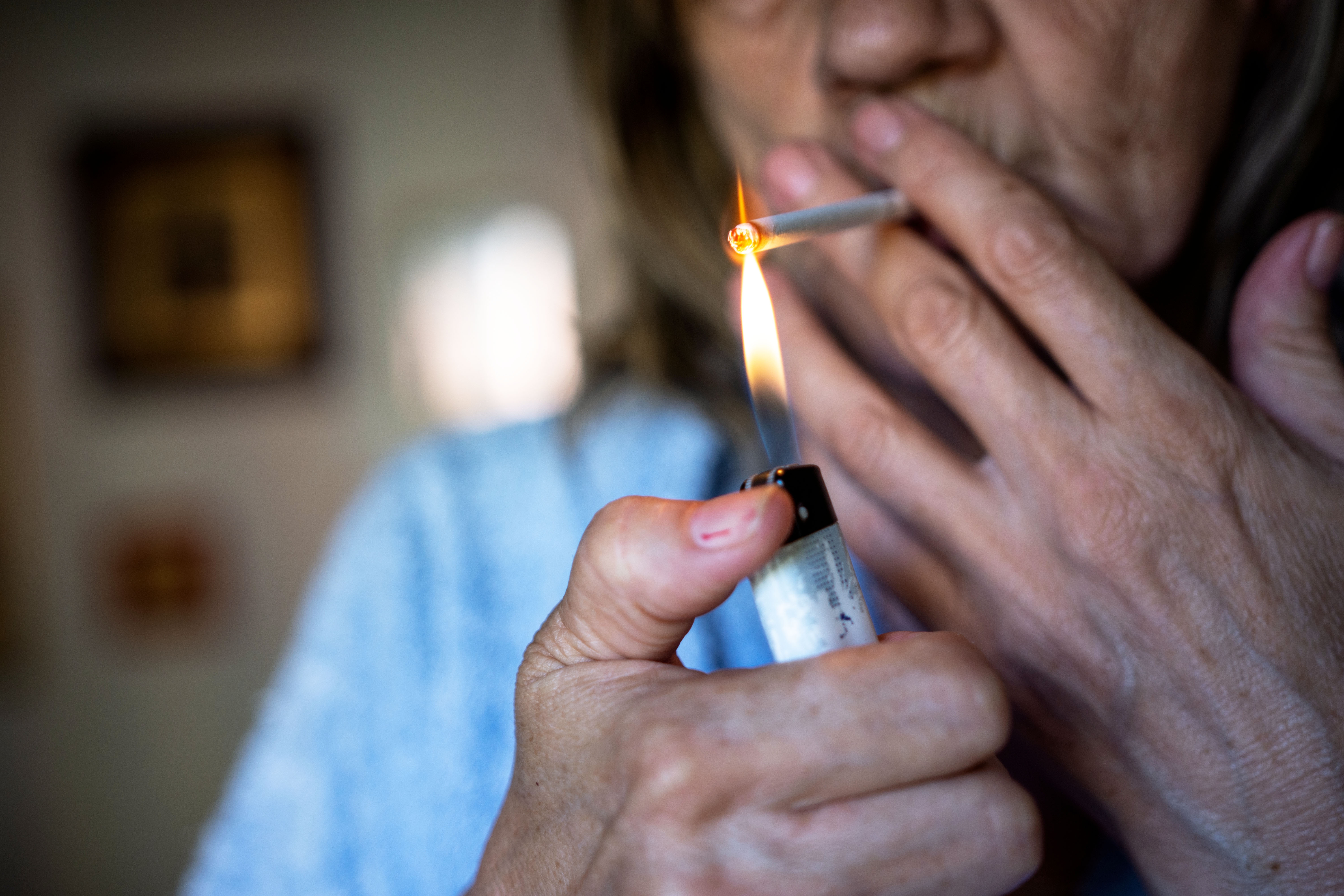 Person lighting a cigarette with a lighter, face partially visible, showing hands and flame