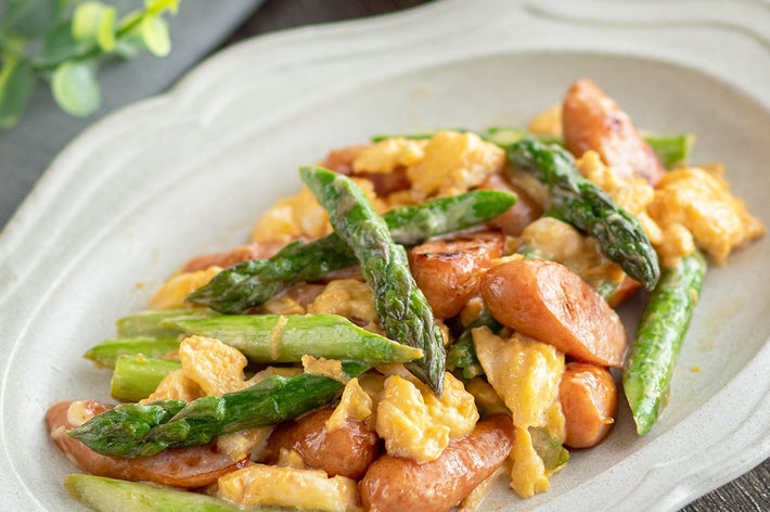 アスパラガスとソーセージ入りスクランブルエッグが皿に盛られている。食卓に並ぶ料理。