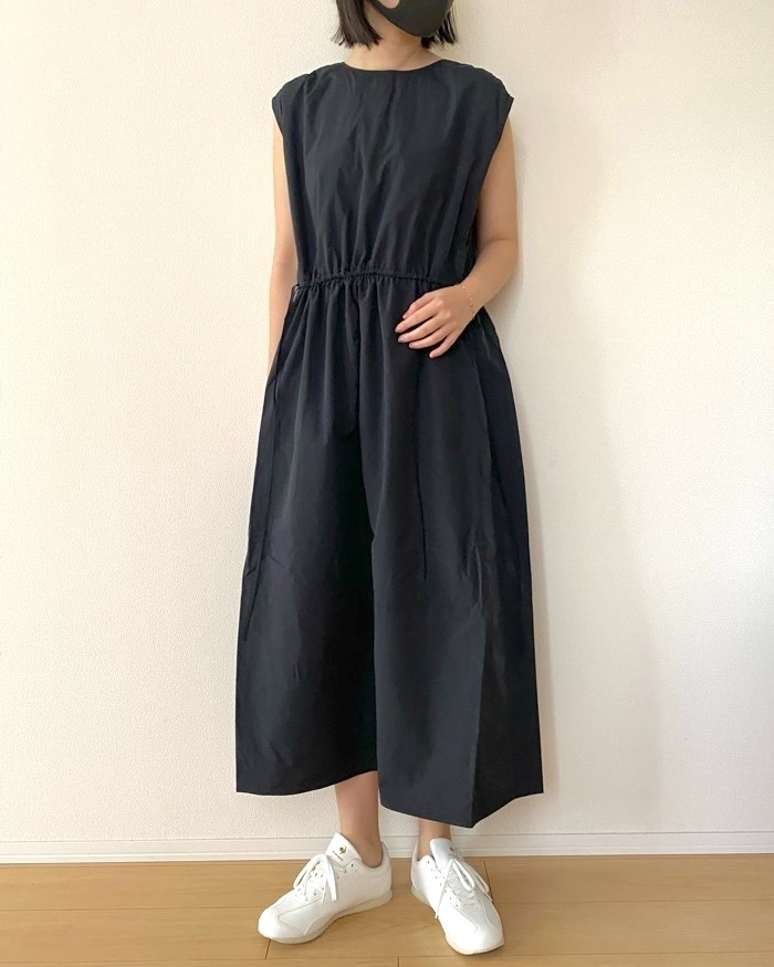 女性が黒のノースリーブジャンプスーツと白いスニーカーを着用。室内で撮影。