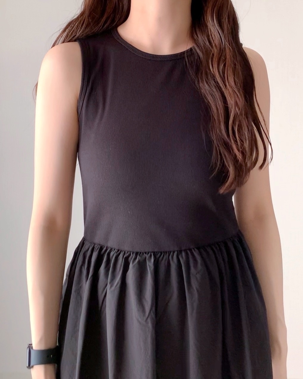 女性がノースリーブのシンプルなドレスを着用している姿。顔は写っていない。