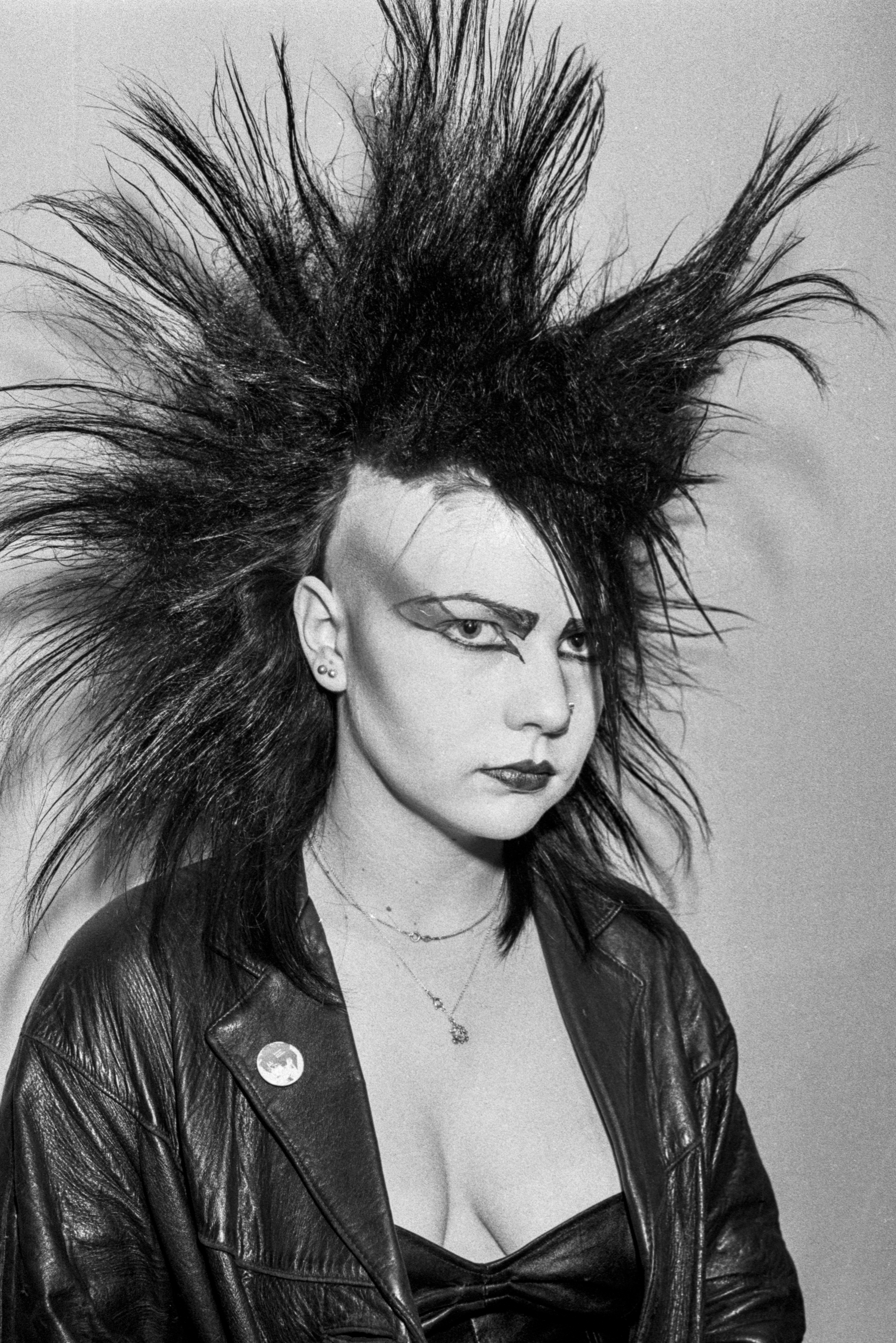 Person with spiked mohawk hairstyle and bold makeup, wearing a leather jacket, showcasing a punk style