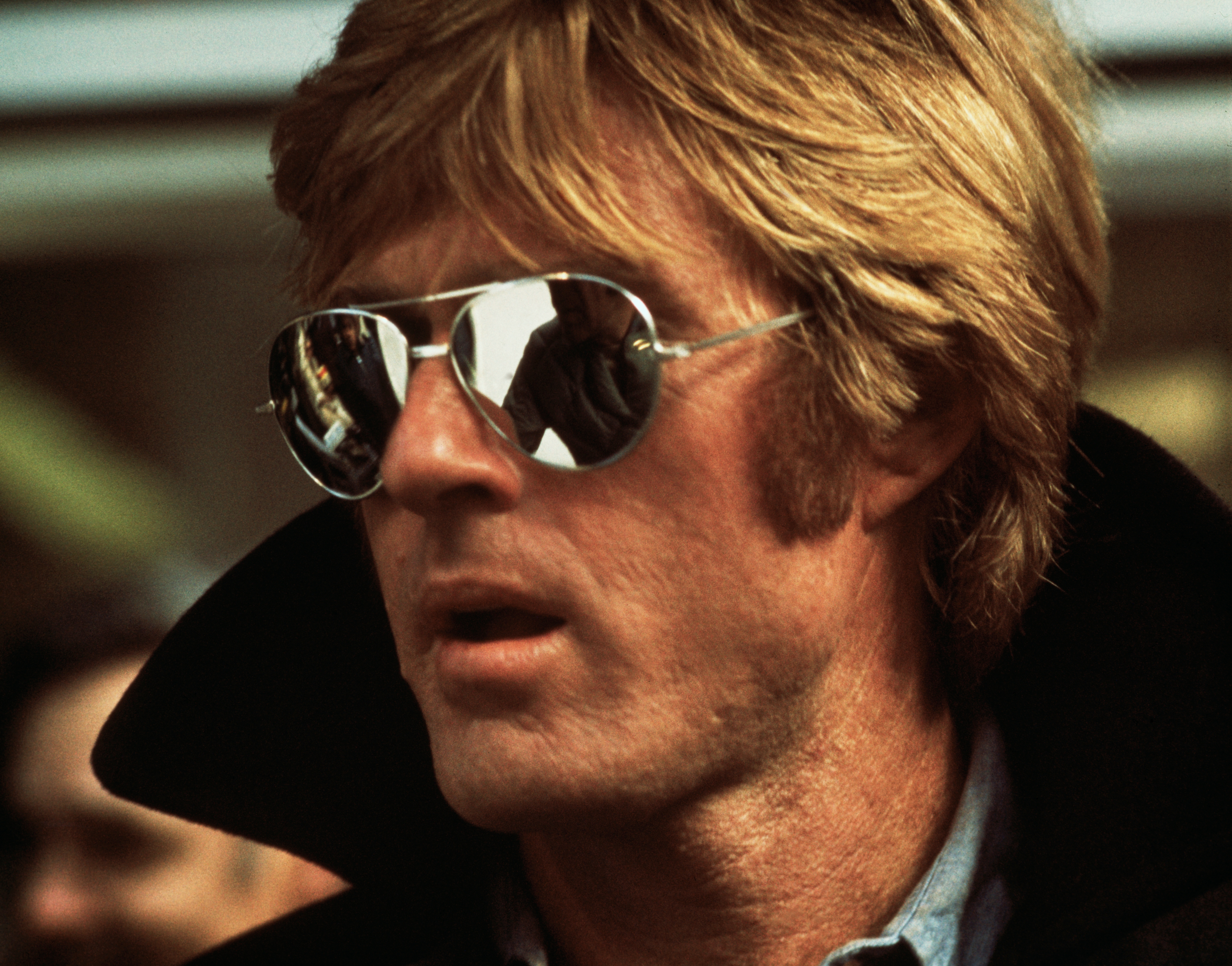 Person wearing aviator sunglasses, looking to the side with a high-collared jacket