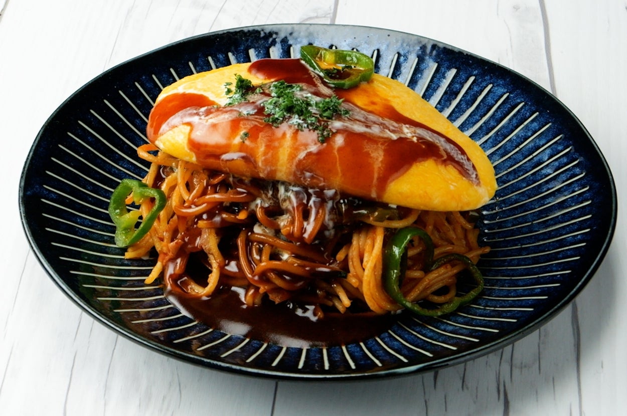 オムレツがスパゲッティの上にのった料理が黒い皿に盛り付けられている。