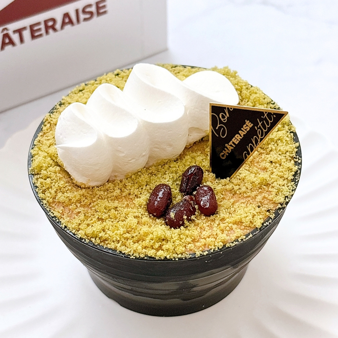 ケーキの上にクリームと小豆が乗ったデザート。トップに金色のロゴが入った三角形のチョコレート装飾がある。