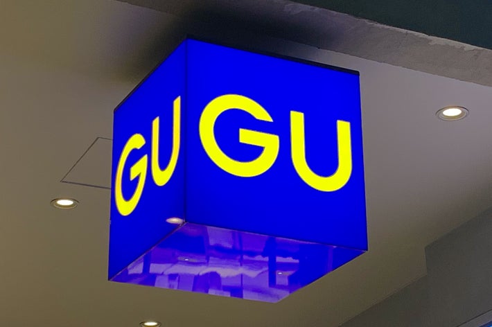 A cube-shaped sign with &ldquo;GU&rdquo; in yellow letters on a blue background hangs from the ceiling